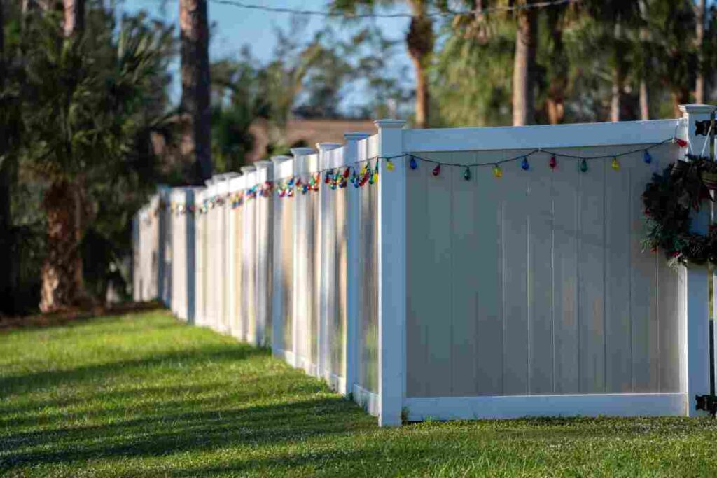 White fence adorned with colorful lights, surrounded by grass and trees in the background.